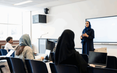 Woman in hijab standing at the front of a classroom talking to her students.