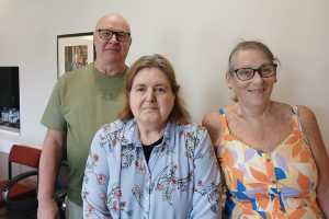 Man (left), woman (middle) and woman (right) standing and smiling for a picture. Chest upwards.
