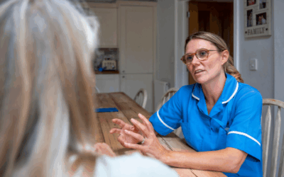 Nurse talking to a woman sat at her table at home. The nurse is explaining something to the woman.