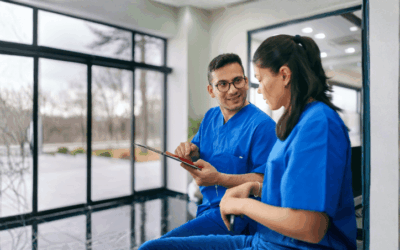 Two nurses in blue uniform having a conversation. The man is showing the woman something on a digital tablet.